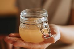 Close-up of a hand holding a glass jar filled with golden liquid on a wooden table.