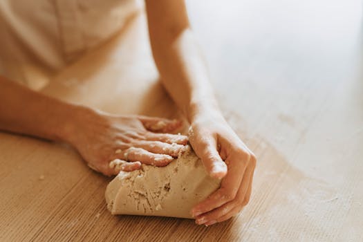 A detailed close-up of hands kneading fresh dough on a wooden table, illustrating the art of baking.