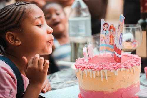 Free Happy little ethnic child blowing out candles during birthday celebration Stock Photo