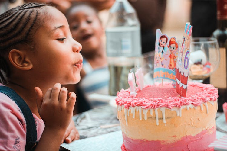 Happy Little Ethnic Child Blowing Out Candles During Birthday Celebration