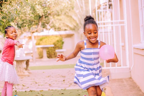 Happy little black children having fun in yard with balloons