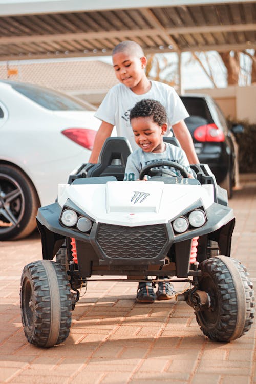 Concentrated ethnic boy helping little brother to drive toy car on street on sunny day