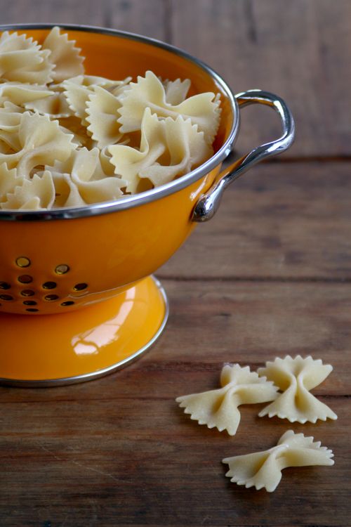Free Close-up of uncooked farfalle pasta in a vibrant yellow strainer on a wooden table. Stock Photo