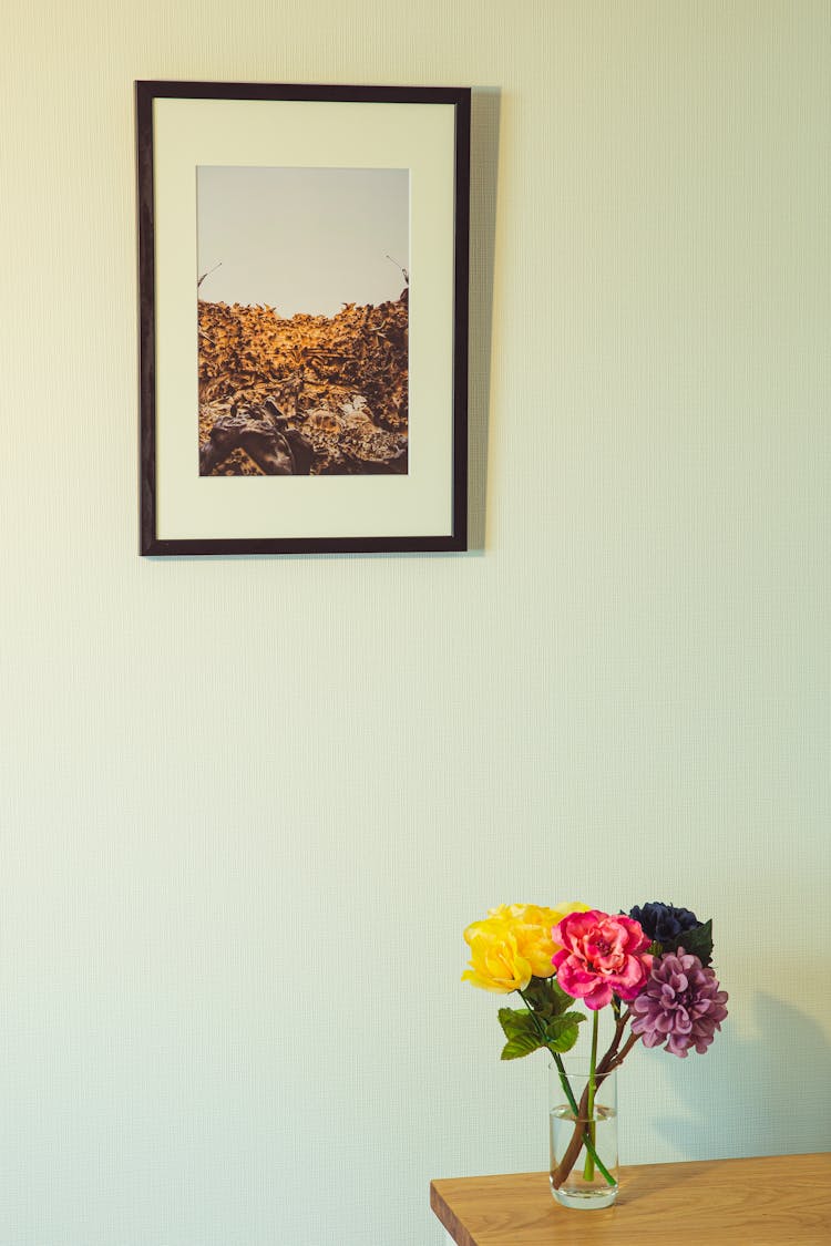 Colorful Flowers In Vase On Wooden Table Placed Near Wall With Framed Photo