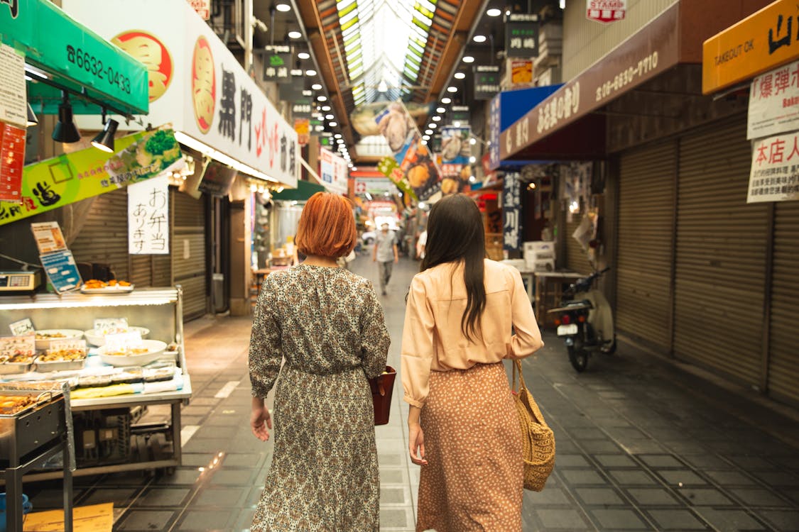 Free Back view of unrecognizable trendy female travelers in stylish clothes walking in traditional famous Nishiki Market in Kyoto Stock Photo