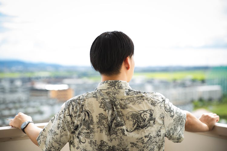 Unrecognizable Man Standing On Open Balcony Against Green City