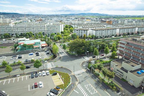 Scenery of contemporary city district with modern apartment buildings and vast parking area amidst green lush trees situated on hilly valley on sunny weather