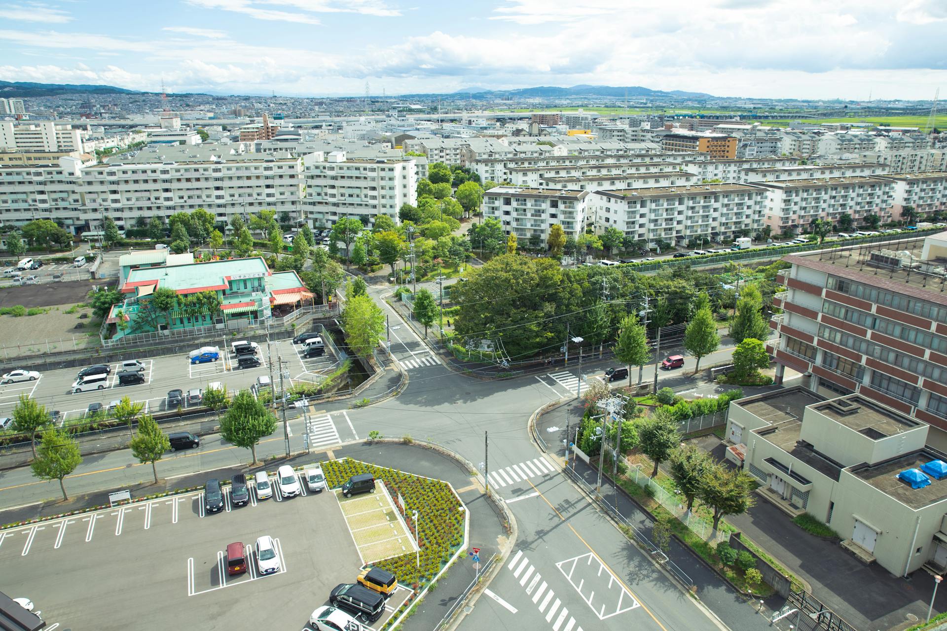 Scenery of contemporary city district with modern apartment buildings and vast parking area amidst green lush trees situated on hilly valley on sunny weather