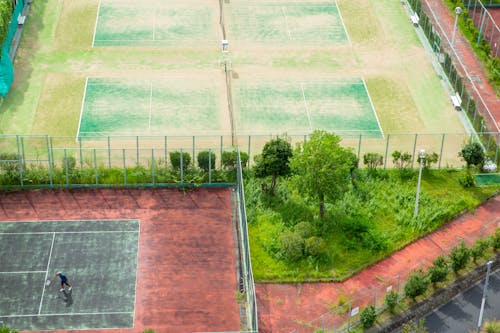 Aerial view of distant person playing tennis on aged weathered tennis courts on lush green meadow