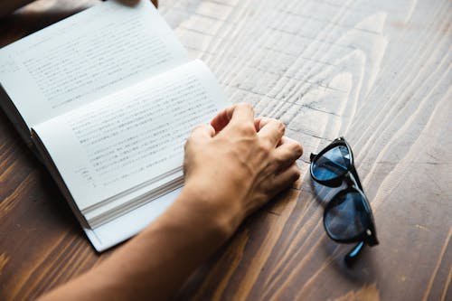 Crop faceless person sitting at table and reading book