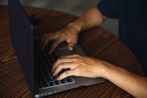 Crop anonymous male in black shirt sitting at round table and working on modern netbook