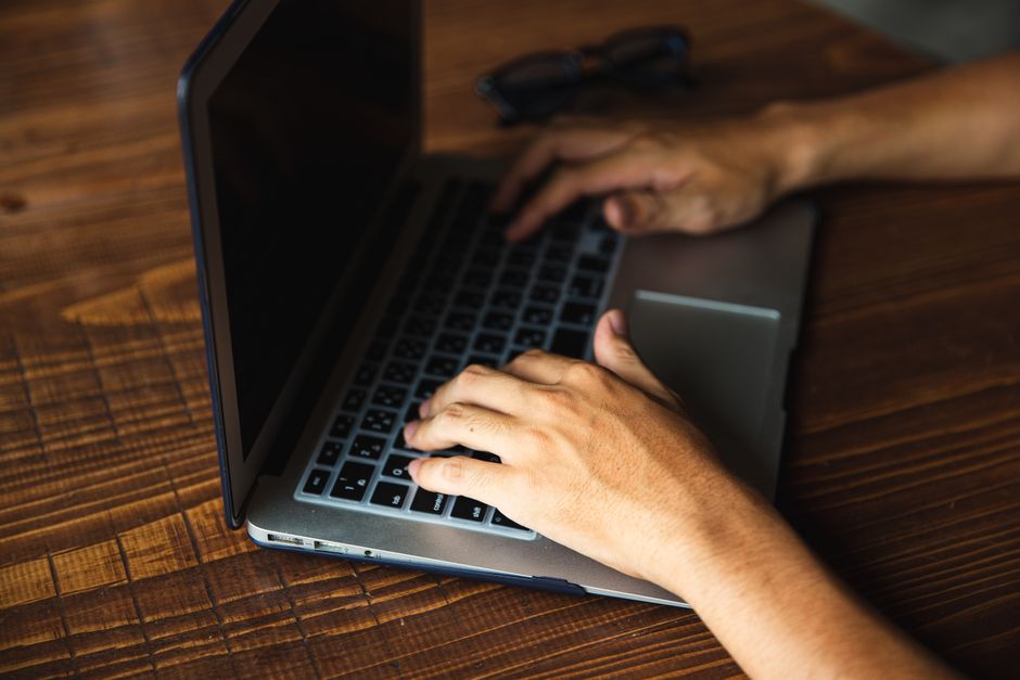 木製の机の上でノートパソコンのキーボードで作業している手のクローズアップ、現代テクノロジーを示す。