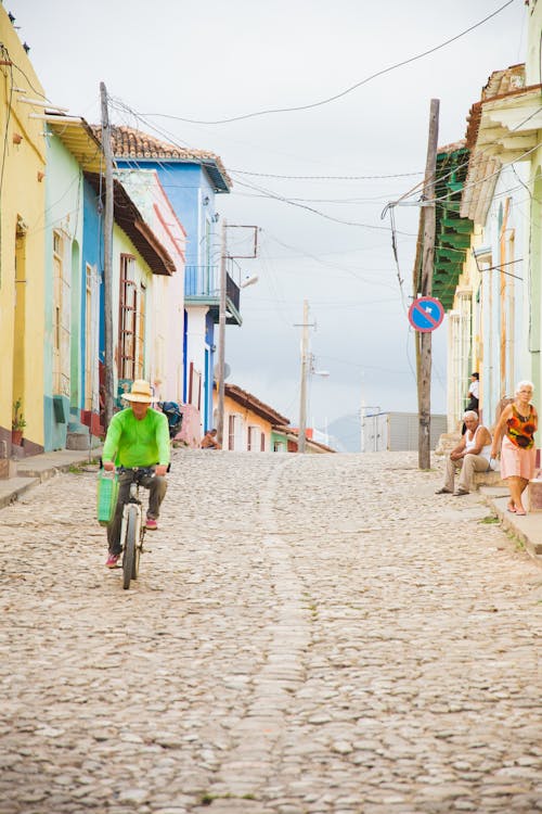 Anonymous male in hat riding bicycle on cobblestone street between aged urban house facades