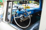 Interior of aged transport with steering wheel and leather seat under mirror reflecting town in daylight