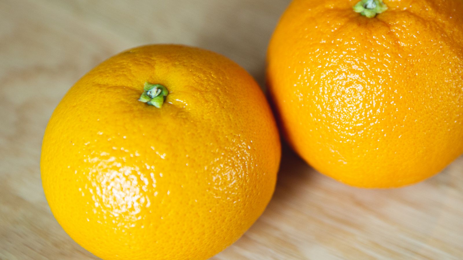Two oranges on a wooden surface in warm light