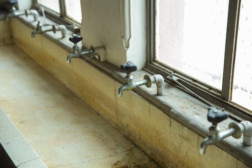 Similar old taps above weathered public sink in building
