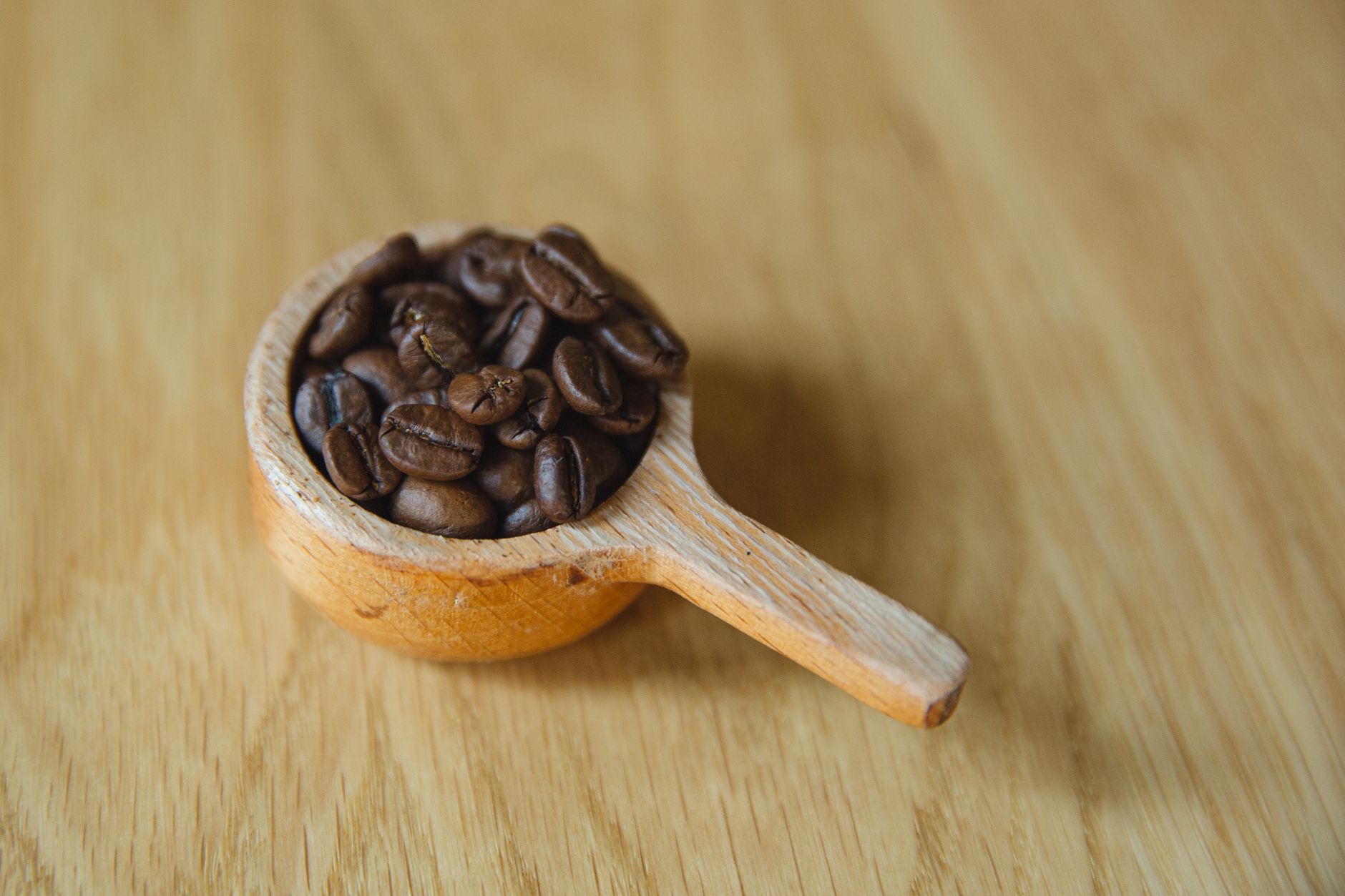 From above of wooden spoon full of roasted coffee beans on wooden surface