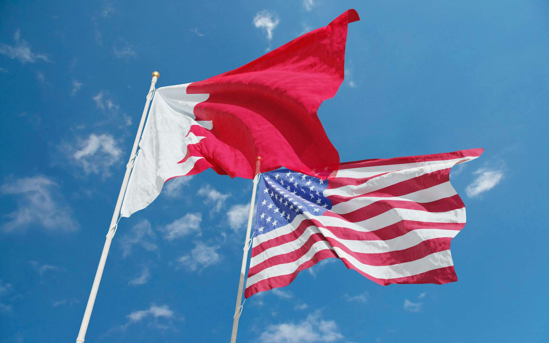 Flags of Bahrain and the United States waving against a bright blue sky, symbolizing international relations.