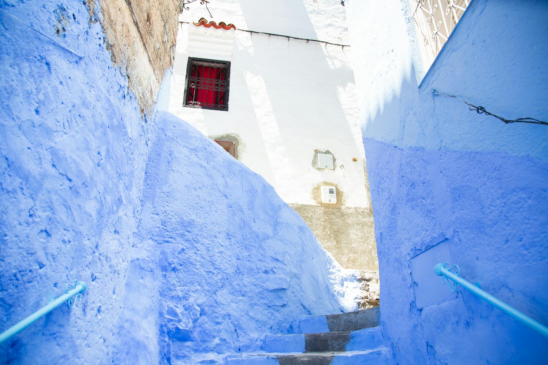 Colorful steps with railings between painted blue walls leading to aged stone residential building on sunny street in old town