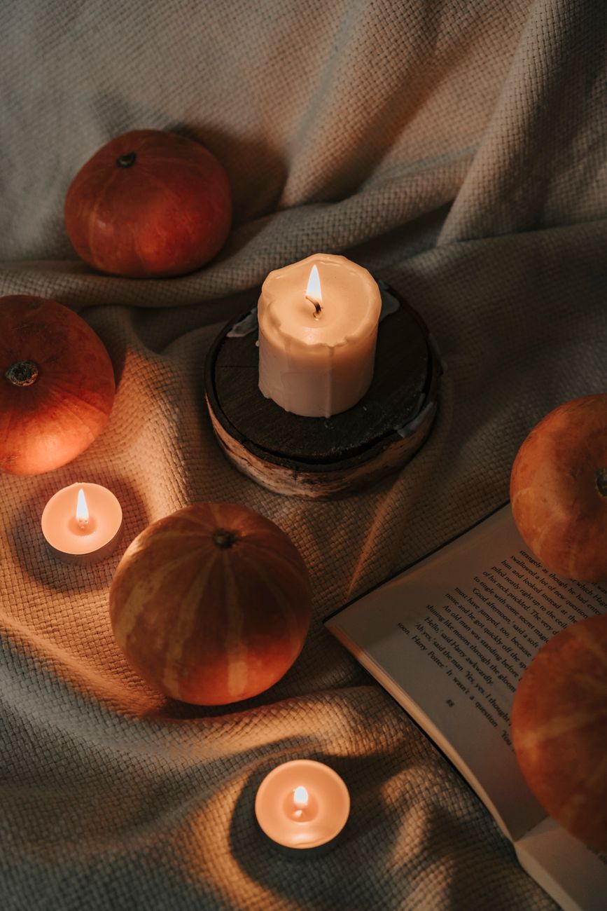 Warm still life featuring lit candles and pumpkins on a textured fabric backdrop, perfect for autumn vibes.