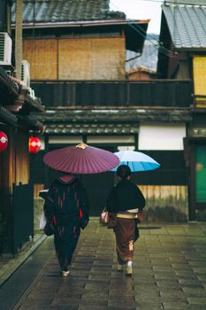 一对穿着传统服装的夫妇撑着彩色雨伞，漫步在京都的街道上
