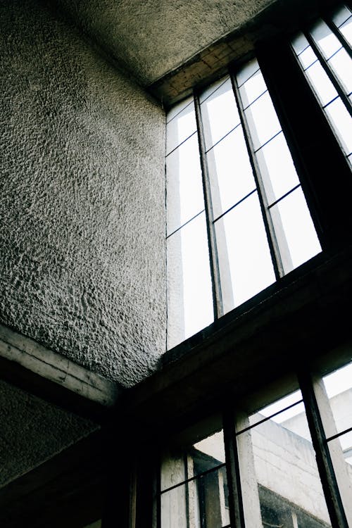 From below big rectangular shaped windows on concrete buildings with uneven walls and ceiling in daylight