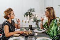 Woman in Black and White Floral Dress Sitting on Chair in Front of Table With Plates