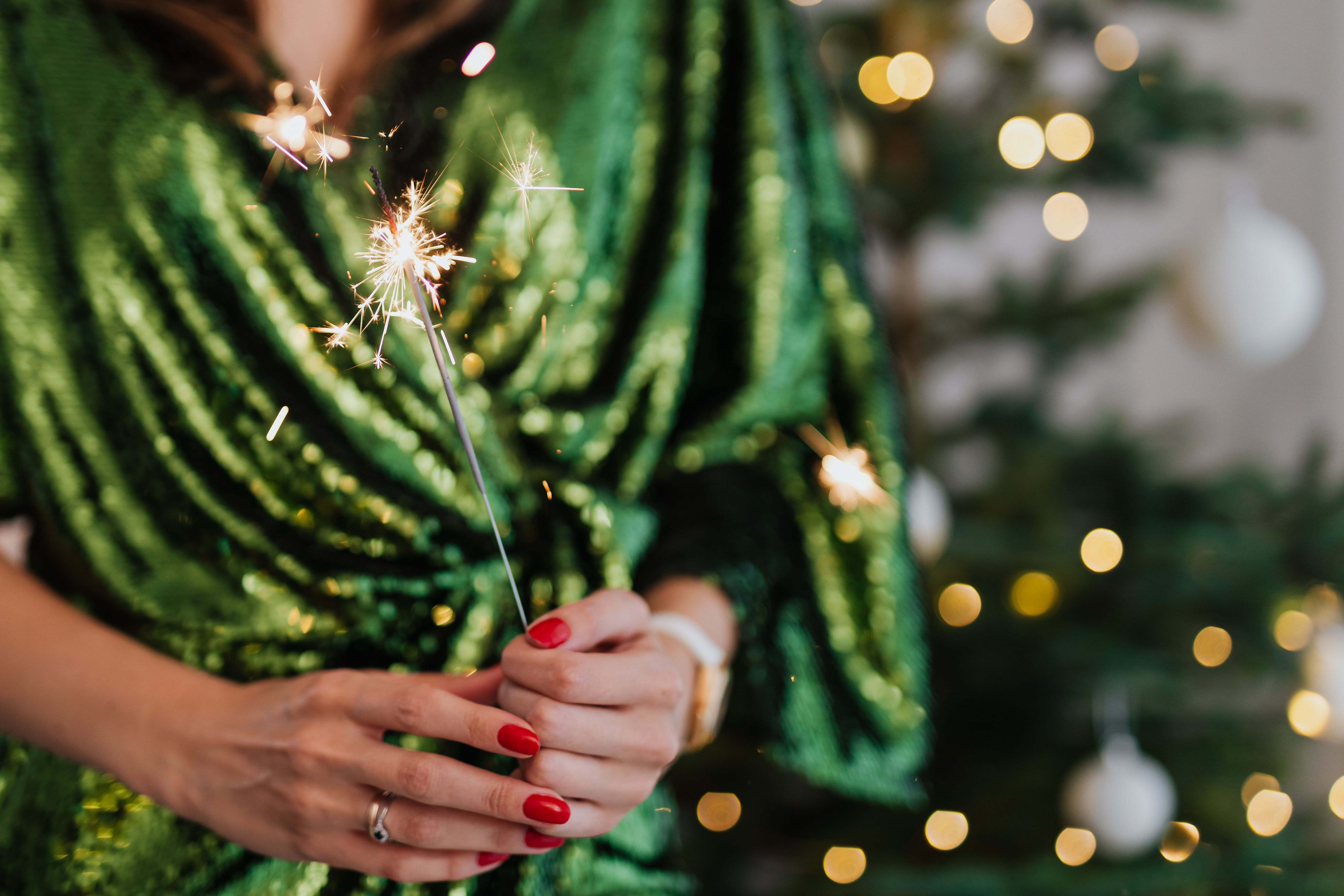 一名身穿绿色连衣裙的妇女在室内手持烟花庆祝圣诞节