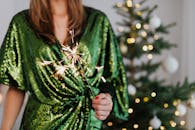 一名身穿绿色连衣裙的妇女在装饰好的圣诞树旁手持烟花，热情庆祝节日