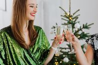 妇女们身着节日服装，在室内的圣诞树旁碰杯起泡酒