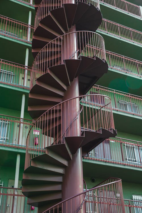 From below of metal spiral stairway located near residential building with green wall in daytime