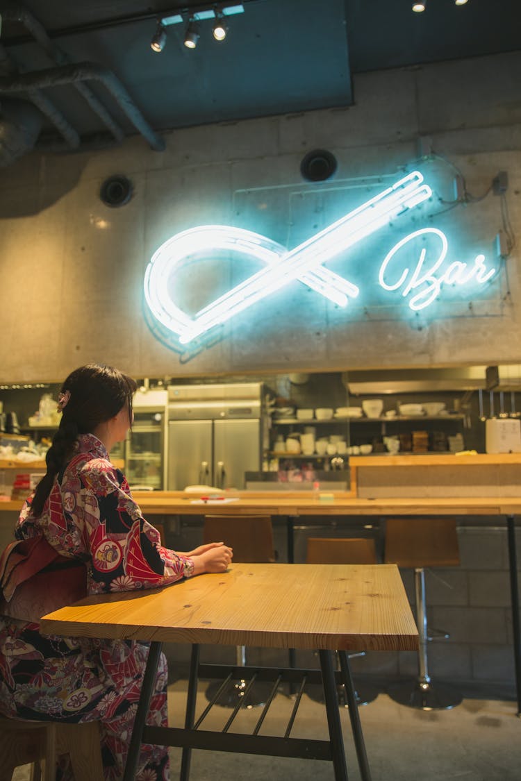 Woman Dressed Like Geisha Sitting At Table In Empty Bar