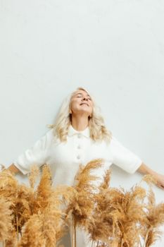 一位金发女子穿着白色毛衣，在干草的簇拥下快乐地拥抱户外