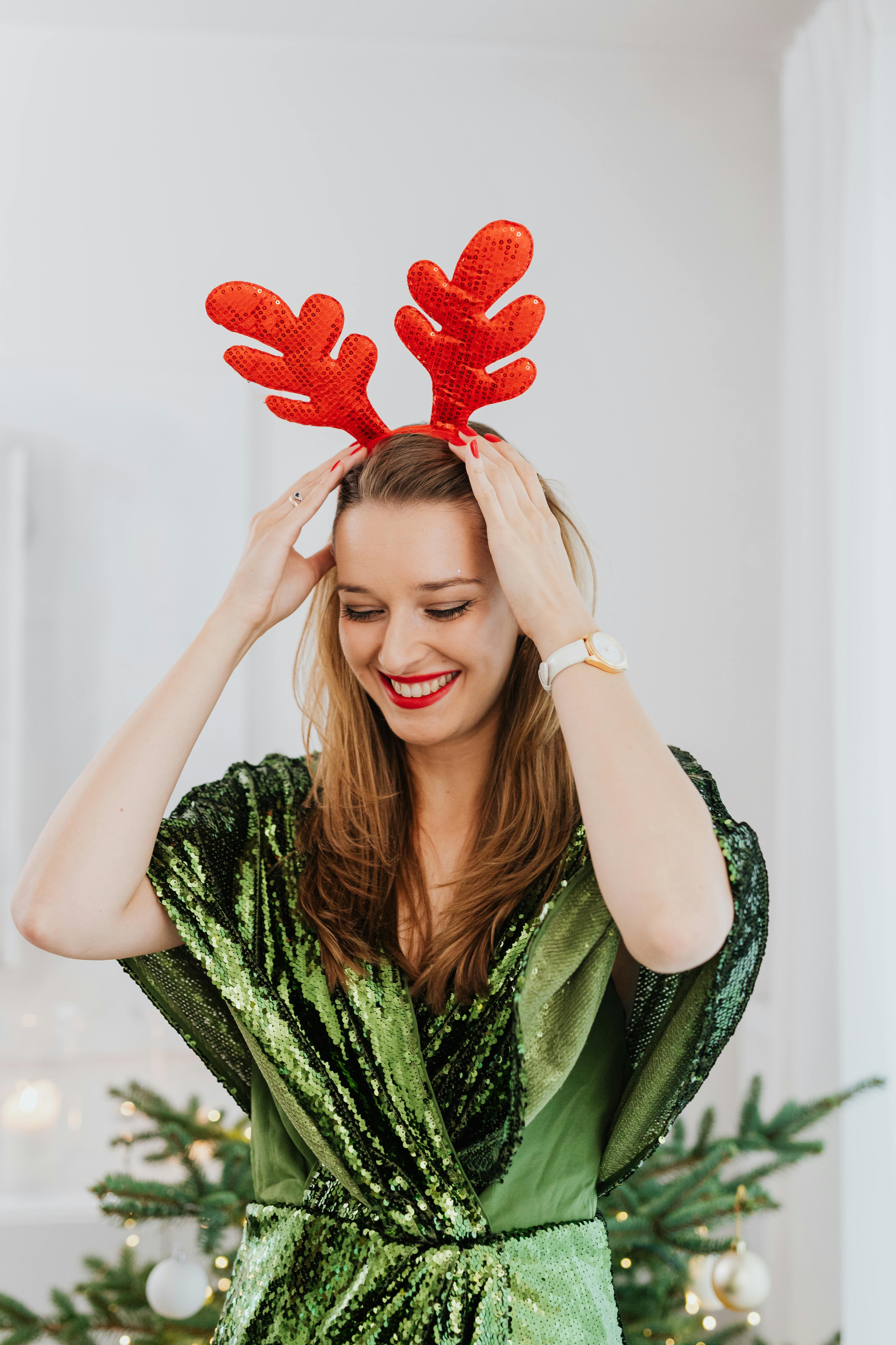 一位快乐的女子身穿喜庆的绿色连衣裙，头戴红色驯鹿发带，正在室内庆祝圣诞节