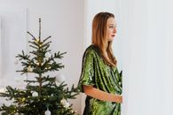 一位穿着亮片绿色连衣裙的优雅女子，在室内一棵装饰精美的圣诞树旁，向窗外望去