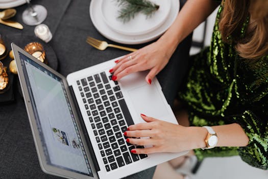 A woman remotely working on a laptop at a beautifully set dinner table with festive decorations.