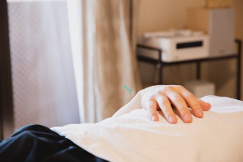 Crop anonymous male client with needle in hand lying on couch during treatment therapy in salon