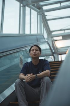 一位穿着休闲服装、戴着手表的年轻亚洲男性，在地铁移动的楼梯上看着镜头