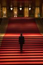 Full body of anonymous dark figure of person walking on stairs in spacious hall with red carpet