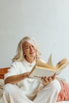 一位白发苍苍的资深女士在舒适的室内环境中享受着阅读一本书的乐趣