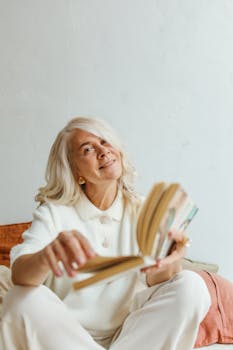 一位白发迷人的资深妇女在室内微笑着阅读，表情温暖