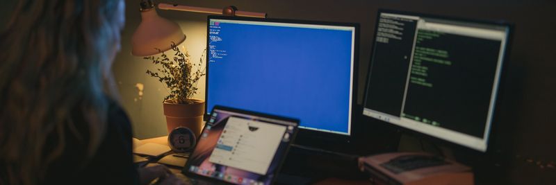 Woman using multiple screens for cybersecurity tasks in a cozy home office