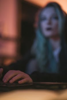 Blurred focus on a young woman typing on a keyboard, captured in a soft, moody lighting setting.