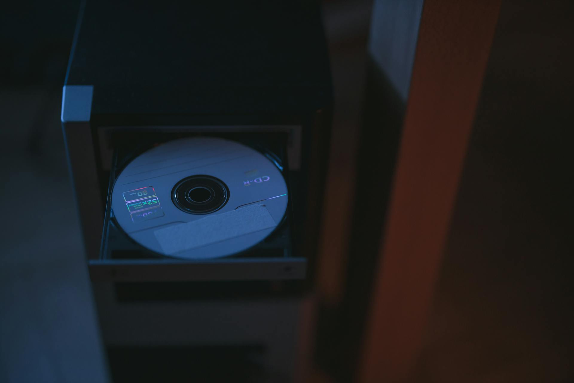 A close-up image of a CD partially ejected from a drive, showcasing soft lighting.