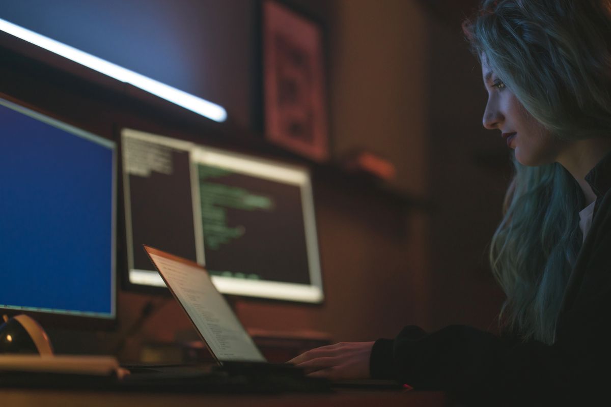 Woman working at a desk with laptops and multiple screens