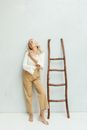 Woman in White Shirt and Brown Pants Standing Beside Brown Wooden Ladder