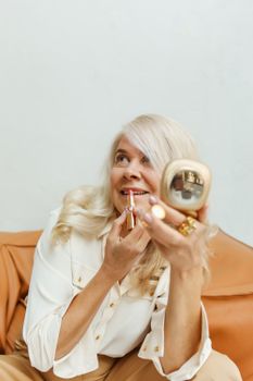 一位白发的高级女性微笑着对着镜子涂口红