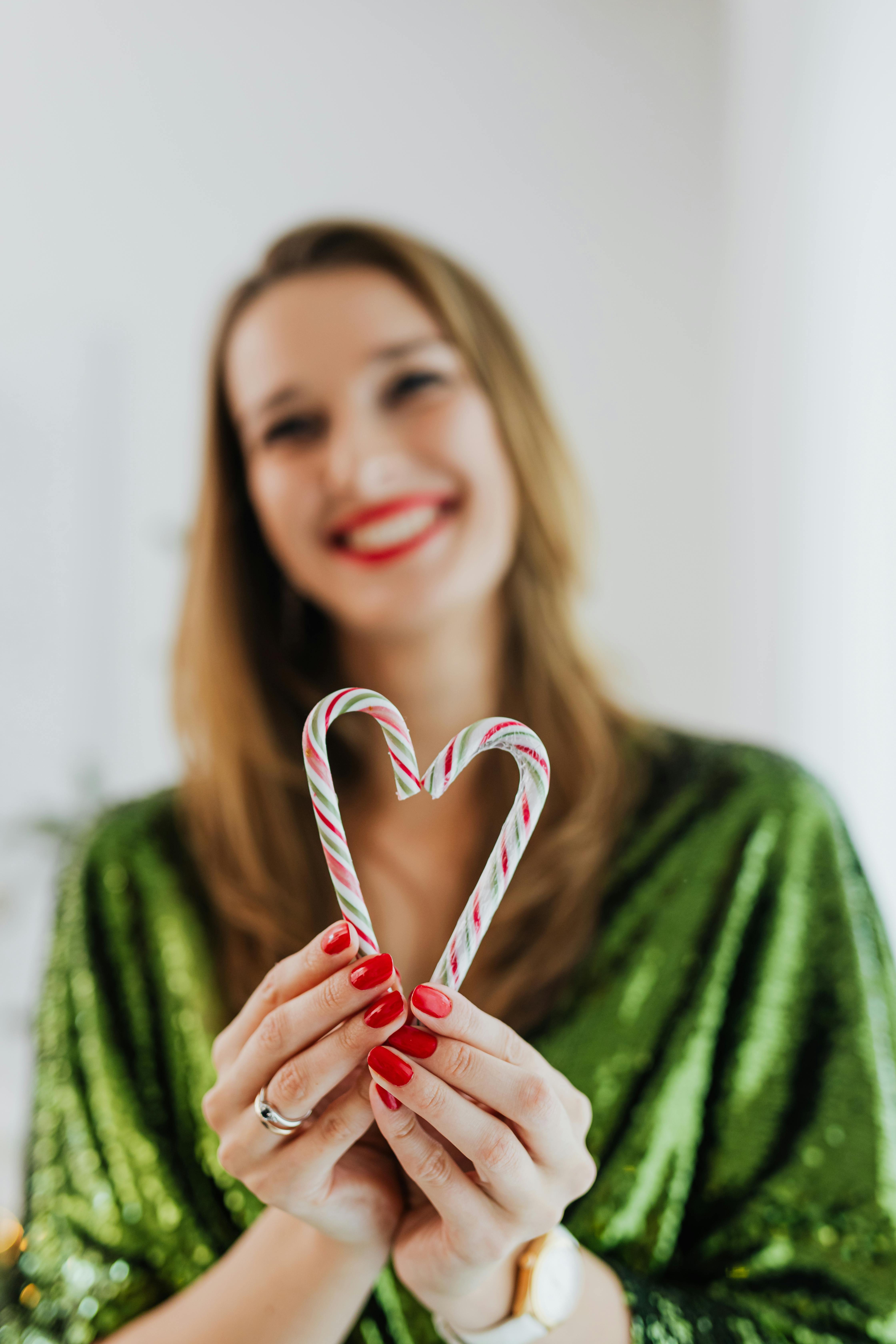 smiling woman holding two candy canes in a heart shape