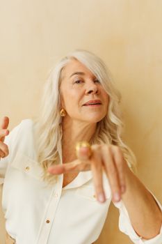 一位优雅的高级女性，留着金色长发，身着白色上衣，在中性背景下摆着姿势