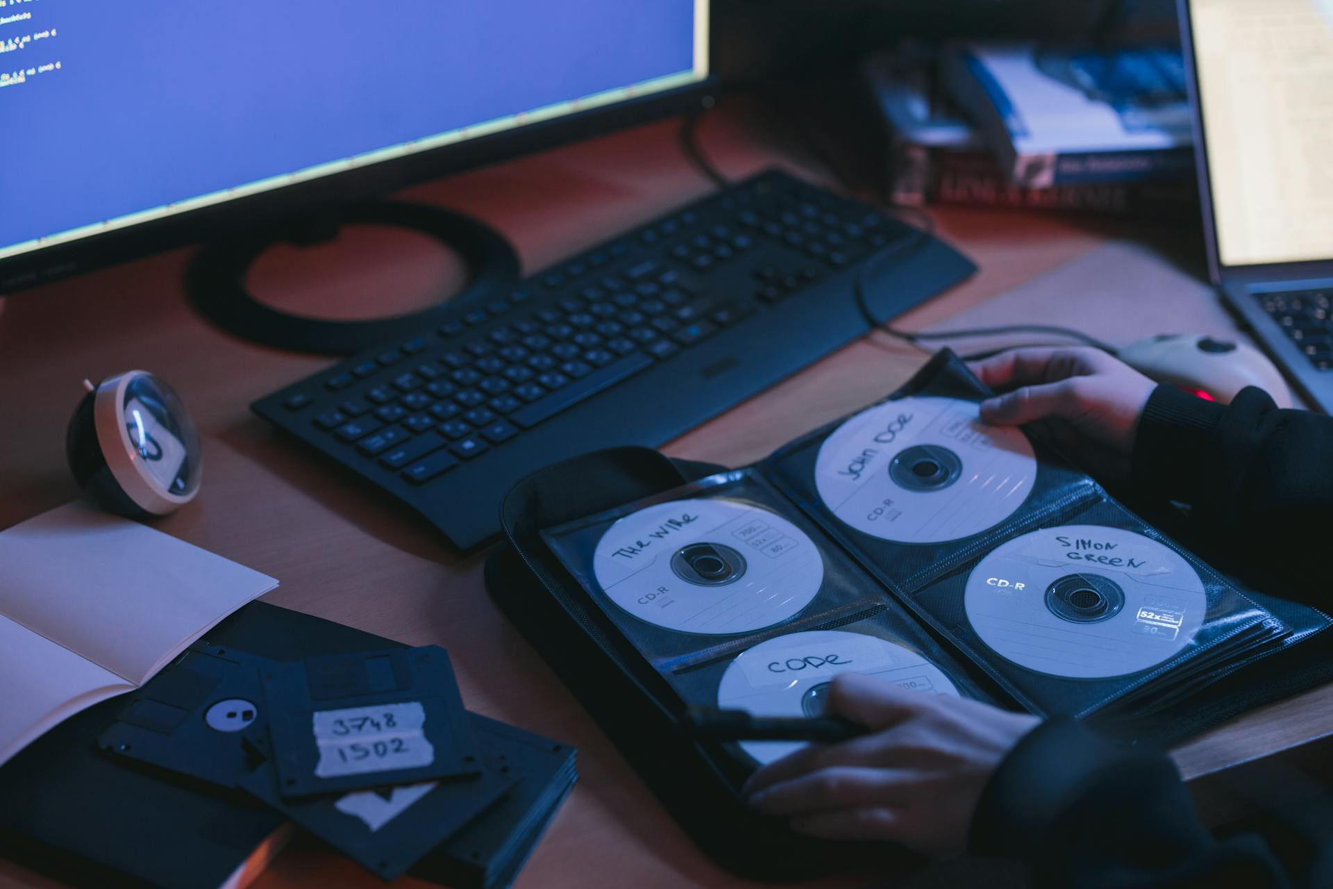 A close-up of CDs and disks on a desk, featuring hands in a tech environment.